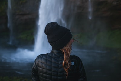 在瀑布附近穿着黑色夹克的女人的照片
